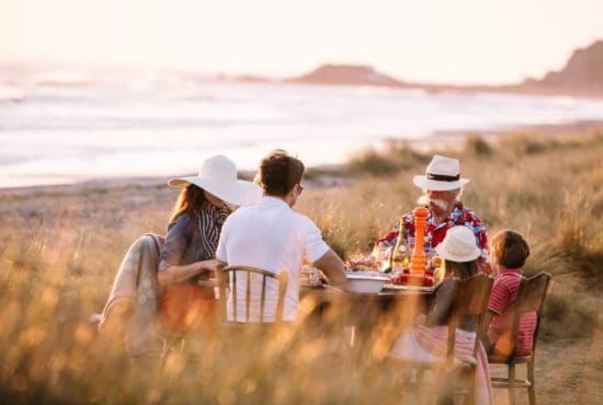 Family eating picnic dinner in sand dunes overlooking beach