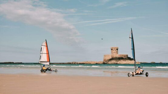 Two people blow karting on Saint Ouens beach in front of Le Rocco tower