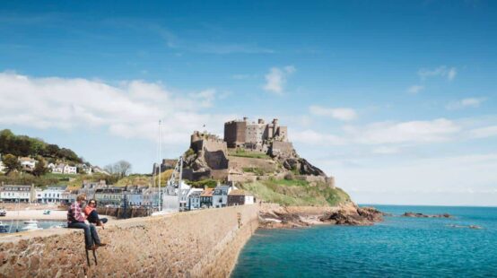 Two people sat on harbour wall in front of Gorey castle