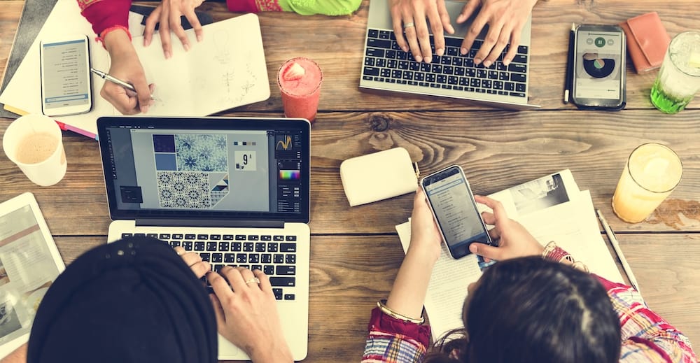 Employees collaborating on work using their phones and laptops remotely in a café 