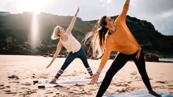 Two women doing yoga on the beach