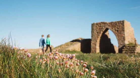 Couple walking in field in front of Grosnez archway