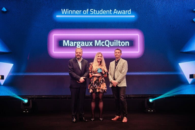 Student Award Winner, Margaux McQuilton, stood on stage with award and host Hal Cruttenden