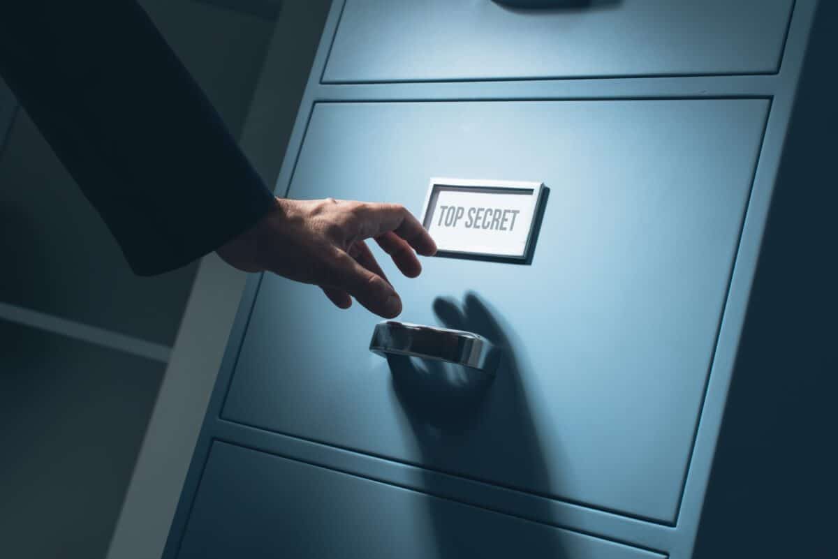 Hand reaching to open a file cabinet labelled 'Top Secret' 